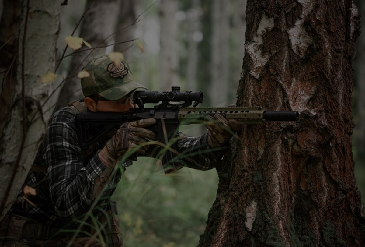 A person in camouflage holding a rifle and aiming it.